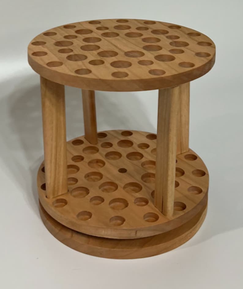 A wooden rotating paintbrush holder with a circular base and a cylindrical center. The holder has many holes to hold paintbrushes. The holder is filled with a variety of paintbrushes with different colored handles and bristles.