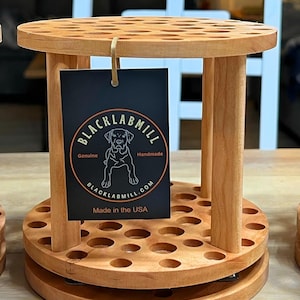 A wooden rotating paintbrush holder with a circular base and a cylindrical center. The holder has many holes to hold paintbrushes. The holder is filled with a variety of paintbrushes with different colored handles and bristles.