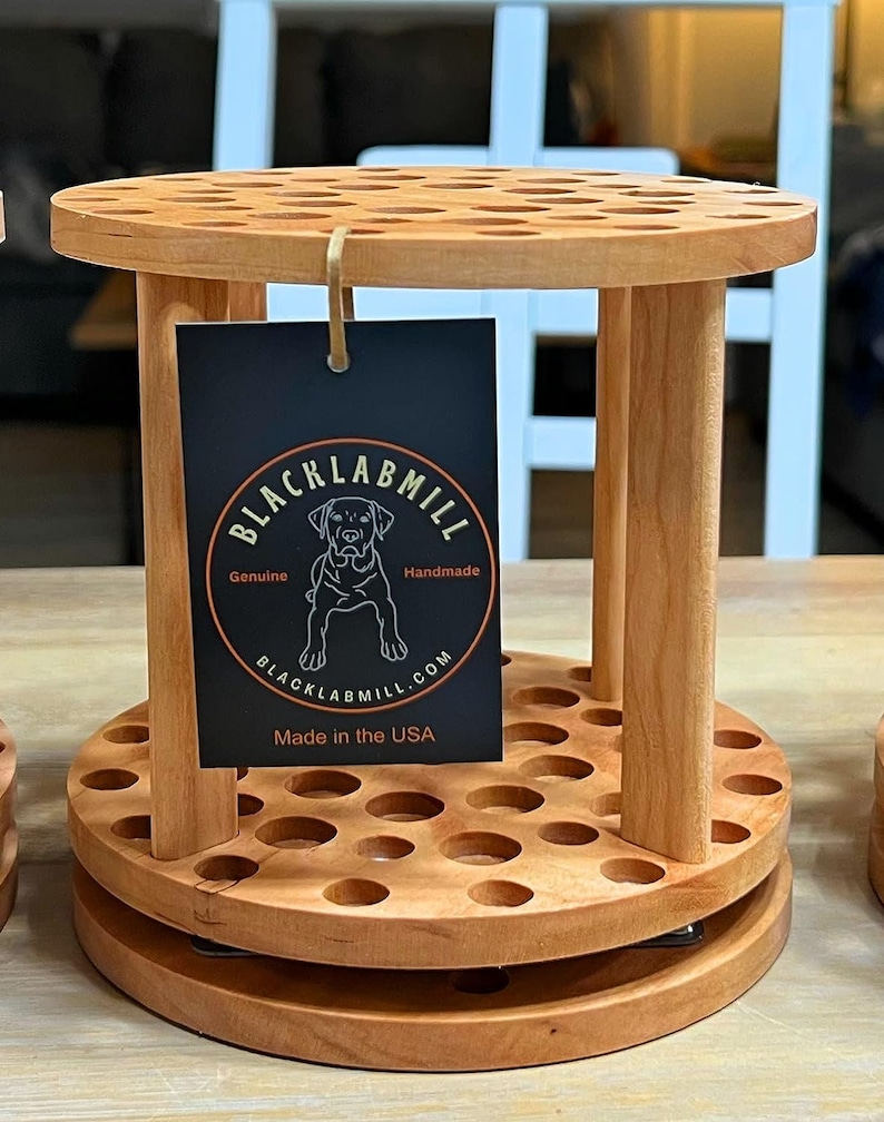 A wooden rotating paintbrush holder with a circular base and a cylindrical center. The holder has many holes to hold paintbrushes. The holder is filled with a variety of paintbrushes with different colored handles and bristles.