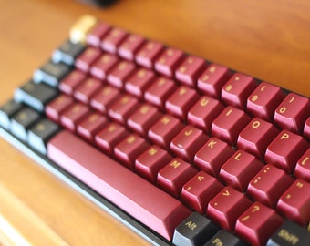 Op de afbeelding: Een rood mechanisch toetsenbord met gouden letters op de toetsen. Het toetsenbord heeft een zwart frame en een rood-zwarte spatiebalk.