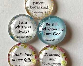 May include: Five circular glass cabochons featuring religious quotes. The top one has yellow floral accents and reads Love is patient, love is kind. Corinthians 13:4. Others include Matthew 28:20, Psalm 46:10, Psalm 136:1, and Joshua 1:9.