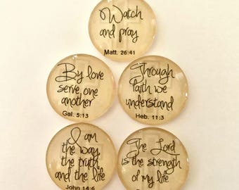 May include: Five round, translucent beige glass cabochons featuring black script text and a faint cross design. The text includes: Watch and pray Matt. 26:41, By love serve one another Gal. 5:13, Through faith we understand Heb. 11:3, I am the way the truth and the life John 14:6, and The Lord is the strength of my life Psa. 27:1.