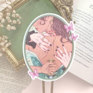 Pu&ograve; includere: Adesivo ovale con un'illustrazione di due figure che si abbracciano, con mani adornate da anelli. L'opera d'arte include un pugnale decorativo e farfalle rosa. L'adesivo &egrave; ambientato sullo sfondo di un libro e di una cornice decorativa.