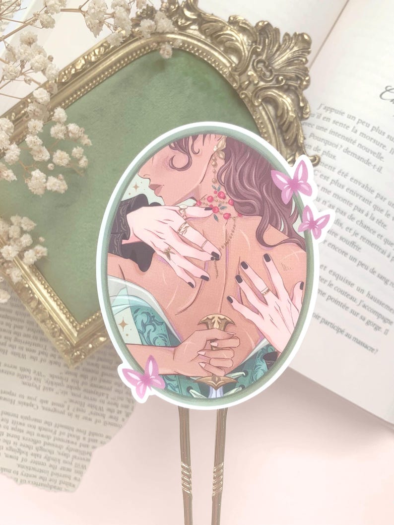 Pu&ograve; includere: Adesivo ovale con un'illustrazione di due figure che si abbracciano, con mani adornate da anelli. L'opera d'arte include un pugnale decorativo e farfalle rosa. L'adesivo &egrave; ambientato sullo sfondo di un libro e di una cornice decorativa.