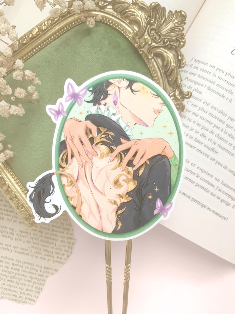 Pu&ograve; includere: Un adesivo decorativo con un'illustrazione di due figure che si abbracciano, all'interno di un cerchio verde. L'opera presenta una figura maschile con capelli scuri e un cappotto nero ornato da accenti dorati. Farfalle e stelle viola decorano il design.