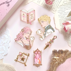 Peut inclure: Collection d'épingles en émail sur le thème romantique. Les épingles présentent des illustrations d'un livre avec le texte "Once Upon a Broken Heart", d'une dague et de personnages d'un homme et d'une femme. La palette de couleurs comprend le rose, l'or et le marron.