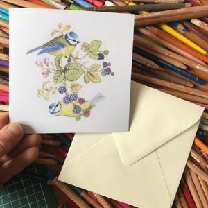 Op de afbeelding: Een wenskaart met een aquarel illustratie van twee pimpelmezen op een tak met bessen en bloemen. Inclusief een crèmekleurige envelop.
