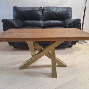Puede incluir: Una mesa de centro de madera con una tapa marrón y patas de metal dorado. Las patas tienen forma de X.