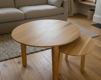May include: A set of two round wooden nesting tables. The larger table is approximately 36 inches in diameter, and the smaller table is about 24 inches in diameter. Both tables have a natural wood grain finish and sturdy, square legs. The tables are in a living room setting.