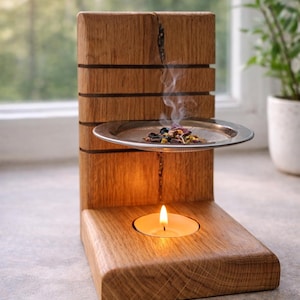 Könnte beinhalten: Ein hölzerner Aromatherapie-Diffusor mit einer brennenden Teelichtkerze an der Basis. Ein kleines Metalltablett enthält getrocknete Kräuter, die duftenden Rauch abgeben. Die Holzstruktur hat eine natürliche Holzmaserung.