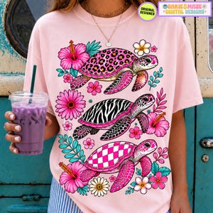 May include: Pink t-shirt featuring three turtles with patterned shells: leopard print, zebra stripes, and a checkered design. The turtles are surrounded by pink hibiscus flowers, daisies, and green leaves. The shirt has the text "ORIGINAL DESIGNER" and "OAKIE & MAZE + DIGITAL DESIGNS".