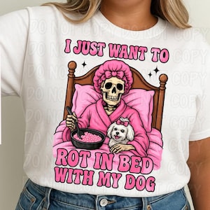 May include: A white t-shirt with a pink skeleton wearing a pink robe and holding a bowl of pink cereal. The skeleton is in bed with a white dog. The text on the shirt reads "I just want to rot in bed with my dog."