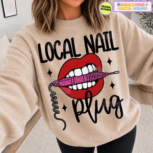May include: A beige crewneck sweatshirt featuring a graphic of red lips holding a pink leopard-print nail drill. The text reads LOCAL NAIL in black block letters above the lips and plug in black script below, accented by small black four-pointed stars.