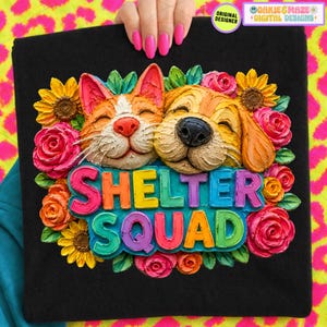 May include: Black tote bag with a colourful design of a cat and dog surrounded by flowers. The text "SHELTER SQUAD" is displayed in vibrant, multi-coloured letters. The design includes the text "ORIGINAL DESIGNER" and "OAKIE & MAZE + DIGITAL DESIGNS".