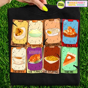 May include: A black sweatshirt featuring eight rectangular tarot-style cards with illustrations of Thanksgiving foods. The cards are labelled: The Deviled Egg, The Potatoes, The Casserole, The Rolls, The Gravy, The Turkey, The Stuffing, and The Pie.