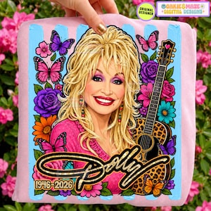 May include: A light pink sweatshirt featuring a graphic illustration of a blonde woman with a guitar, surrounded by colorful butterflies and flowers. The text "Dolly" is written in gold script, with "1946-2026" printed below in gold.