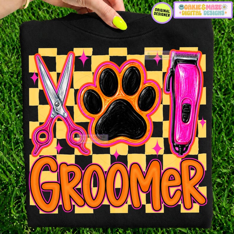 May include: A black sweatshirt featuring a yellow and black checkered pattern background. The design includes a pair of silver grooming scissors, a black paw print, and a pink electric hair clipper. The word GROOMER is printed in orange.