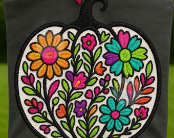 Puede incluir: Tela negra con un diseño de calabaza blanca bordada con flores y hojas coloridas. La calabaza tiene un tallo negro y está llena de flores naranjas, rosas, moradas y turquesas. El texto "OAKIE&MAZE + DIGITAL DESIGNS" está en la esquina superior derecha.