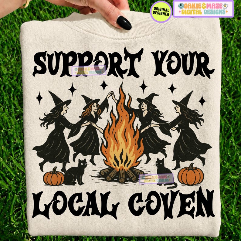 May include: A cream-colored sweatshirt featuring a black graphic print of four witches dancing around a central bonfire. The text reads SUPPORT YOUR LOCAL COVEN in a stylized black font. Two black cats and two orange pumpkins are at the base.