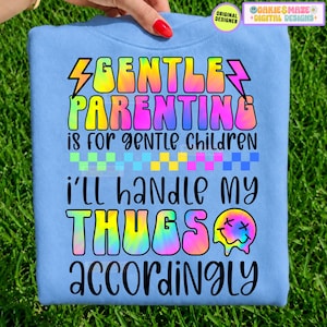 Puede incluir: Una sudadera azul claro con un gráfico tie-dye colorido que incluye el texto GENTLE PARENTING IS FOR GENTLE CHILDREN, un patrón de cuadros, el texto I'LL HANDLE MY THUGS ACCORDINGLY y un icono de cara sonriente derritiéndose.