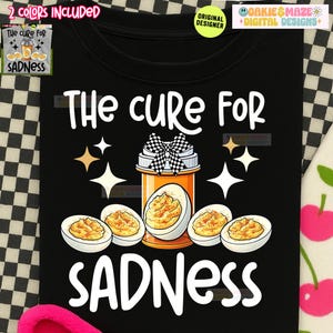 May include: Black t-shirt with the text "The Cure For Sadness." The design features a pill bottle with a checkered bow, surrounded by deviled eggs and star accents. The shirt also includes the text "The Cure For Sadness."