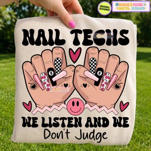 May include: A beige sweatshirt featuring a graphic of two hands with long manicured nails, decorated with cherry patterns, checkerboard prints, and an eight-ball design. The text reads NAIL TECHS WE LISTEN AND WE Don't Judge with a pink smiley face.