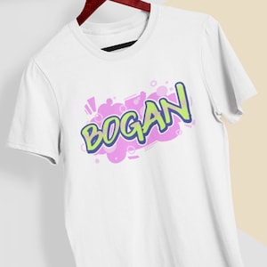 May include: White t-shirt with a graphic print of the word "BOGAN" in a colorful comic book style.