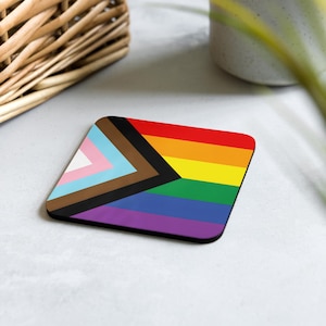 Op de afbeelding: Een vierkante onderzetter met een kleurrijk ontwerp met een regenboogvlag met een zwarte en bruine driehoek in de hoek. De onderzetter is gemaakt van een duurzaam materiaal en is perfect om oppervlakken te beschermen tegen morsen en hitte.