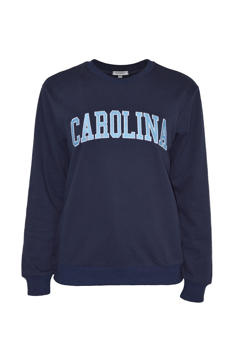 Puede incluir: Sudadera azul marino de cuello redondo con la palabra "CAROLINA" en letras may&uacute;sculas azul claro en el pecho. La sudadera tiene mangas largas y dobladillo y pu&ntilde;os de canal&eacute;. Un dise&ntilde;o sencillo y cl&aacute;sico.