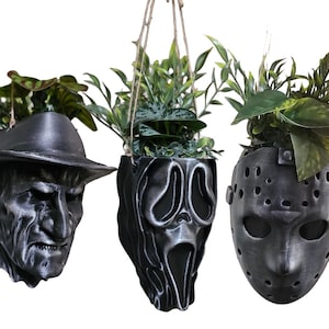 Peut inclure: Trois jardinières suspendues en forme de personnages de films d'horreur : le visage de Freddy Krueger, le masque de Ghostface et le masque de Jason Voorhees. Chaque pot est rempli de plantes vertes et suspendu par de la ficelle.