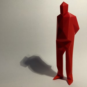 Peut inclure: Une sculpture géométrique rouge en 3D d'une personne debout, les bras croisés. La sculpture est composée de nombreux petits triangles et a un aspect pointu et angulaire.