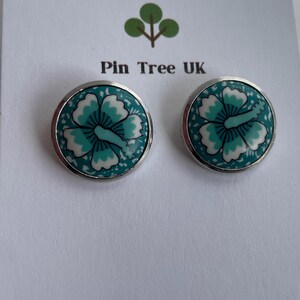 May include: A pair of round earrings with a silver border, featuring a teal and white floral pattern. The earrings are displayed on a white card with the text "Pin Tree UK" and a tree logo.