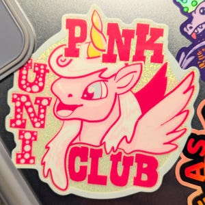 May include: Pink unicorn with wings and a yellow horn, with the text "PINK UNICORN CLUB" in pink letters on a white background with glitter.