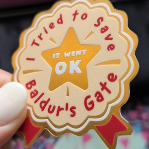 May include: A gold and cream-colored sticker with the text "I tried to save Baldur's Gate" in red, and "IT WENT OK" in white. The sticker has a star in the center and red ribbon accents.