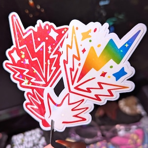 May include: Two holographic stickers featuring a lightning bolt design. One sticker is red with white stars and the other is rainbow with blue stars.