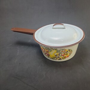 Puede incluir: Cacerola de esmalte blanco con asa marrón y tapa. La cacerola tiene un diseño floral con peras amarillas, bayas rojas y champiñones marrones.