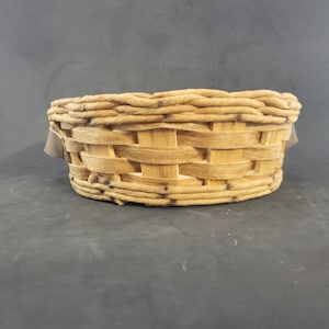 Puede incluir: Una cesta redonda tejida de color marrón claro. Presenta un borde trenzado y un cuerpo tejido. El diseño de la cesta es sencillo y rústico, adecuado para diversos usos. Fabricada con materiales naturales.