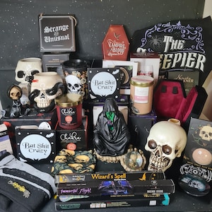 Op de afbeelding: Een verzameling gotische voorwerpen, waaronder schedelvormige mokken, kaarsen met het label Chakra en Wild Rose, wierookstokjes met het label Wizard's Spell en Immortal Flight, een zwart figuur met capuchon en borden met Strange and Unusual.