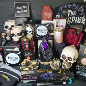 Può includere: Una collezione di oggetti a tema gotico che include tazze a forma di teschio, una figura nera incappucciata con una luce viola, bastoncini di incenso etichettati Wizard's Spell e Immortal Flight, una scatola a forma di bara e cartelli con scritto Strange and Unusual e Bat Shit Crazy.
