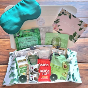 Könnte beinhalten: Eine Geschenkbox mit Pflegeprodukten. Enthält eine türkisfarbene Augenmaske, Gesichtsmasken, Teebeutel, Pralinen und eine Kerze. Die Box enthält eine Karte mit der Aufschrift "Just to Say".