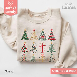 May include: A sand-colored crewneck sweatshirt featuring a graphic print of twelve distinct Christmas-themed icons arranged in a grid, including various stylized evergreen trees, a red cross, and decorative bows in red, green, and gold.