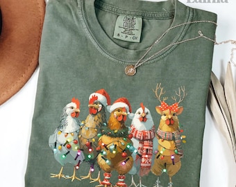 May include: Moss green Comfort Colors t-shirt featuring a festive design of five chickens adorned with Christmas lights and holiday accessories. The chickens wear Santa hats, scarves, and antlers. The shirt has the text "love Lainia".