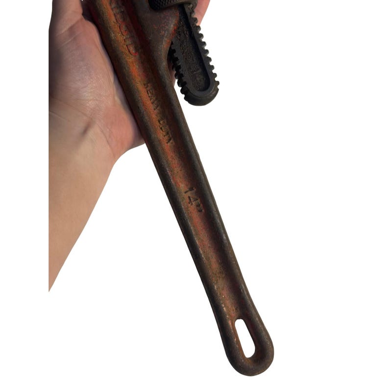May include: A well-worn pipe wrench, with a 14-inch capacity (approx. 35.5 cm). The wrench is a rusty reddish-brown colour, showing signs of use. The adjustable jaw is black, and the handle has a loop at the end.