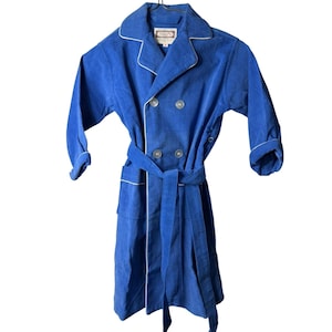 May include: A blue corduroy robe with white trim and a matching belt. The robe has a double-breasted closure with four buttons and a label that reads "Mac's". The robe is hanging on a hanger.