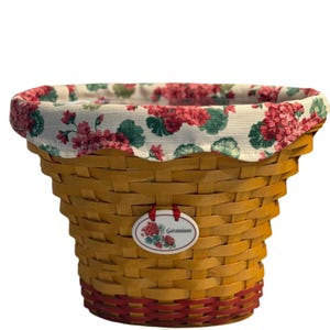 May include: Woven basket with a floral fabric lining featuring red geraniums and green leaves on a cream background. The basket has a red band at the base and a tag that reads "Geranium".