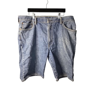 May include: Light blue denim shorts hanging on a black hanger. The shorts have a classic five-pocket design, a button and zipper closure, and belt loops. The denim has a faded appearance.