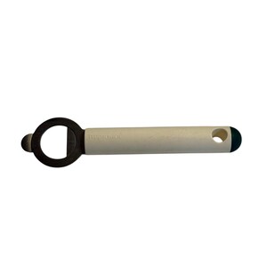 May include: A Tupperware bottle opener with a cream-colored handle and a dark gray opener. The handle has a small hole at the end and the word "Tupperware" printed on it. The end of the handle is dark green.