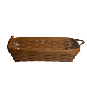 May include: A rectangular woven wooden basket with a medium brown finish, featuring a clear plastic liner insert and two small, curved wooden handles attached to the sides. The basket has a classic woven construction with visible horizontal strips.
