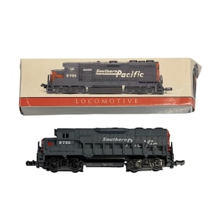 May include: A gray model train locomotive with the number 9725 and the words "Southern Pacific" printed on the side. The locomotive is displayed next to its original box, which also features the train.