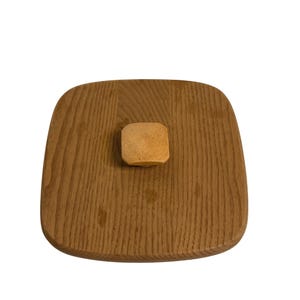 May include: A square wooden lid with rounded corners and a small, square wooden knob. The lid is made of light brown wood with a visible wood grain pattern. The knob is a lighter shade of brown.